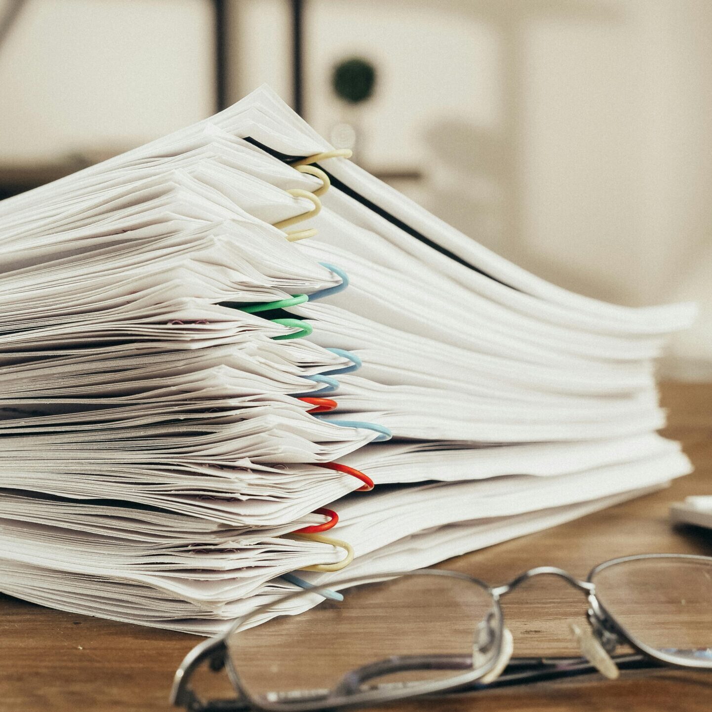 Close-up of a stack of office papers on a desk with glasses, emphasizing organization.